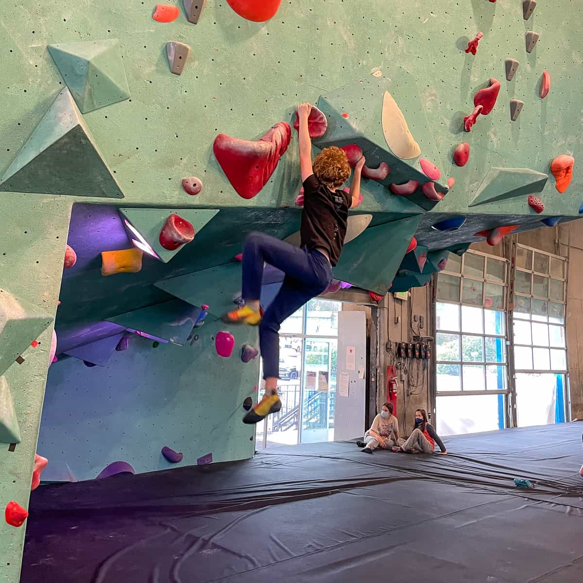 bouldering on overhang over wall to wall padding in climbing gym